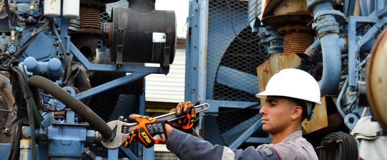 Trabalhador com luvas KPN KEV resistência ao corte ANSI A9 e capacete branco operando chave inglesa em equipamento industrial pesado.